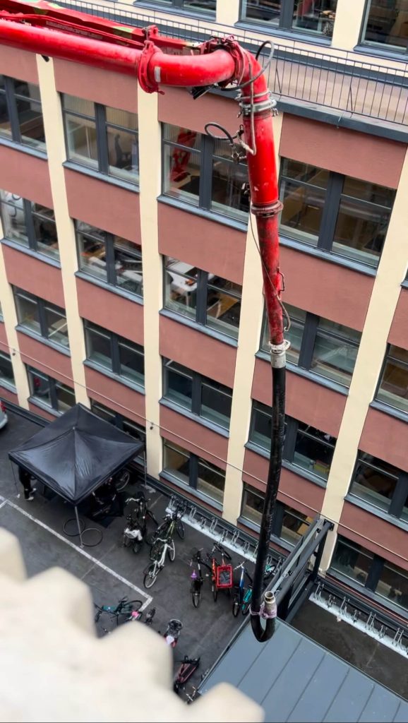 Betongpump med utfälld bom längs fasaden på en flervåningsbyggnad