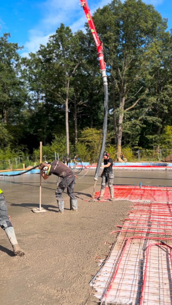 Betongpumpens bom når in över en platta medan betongen dras av