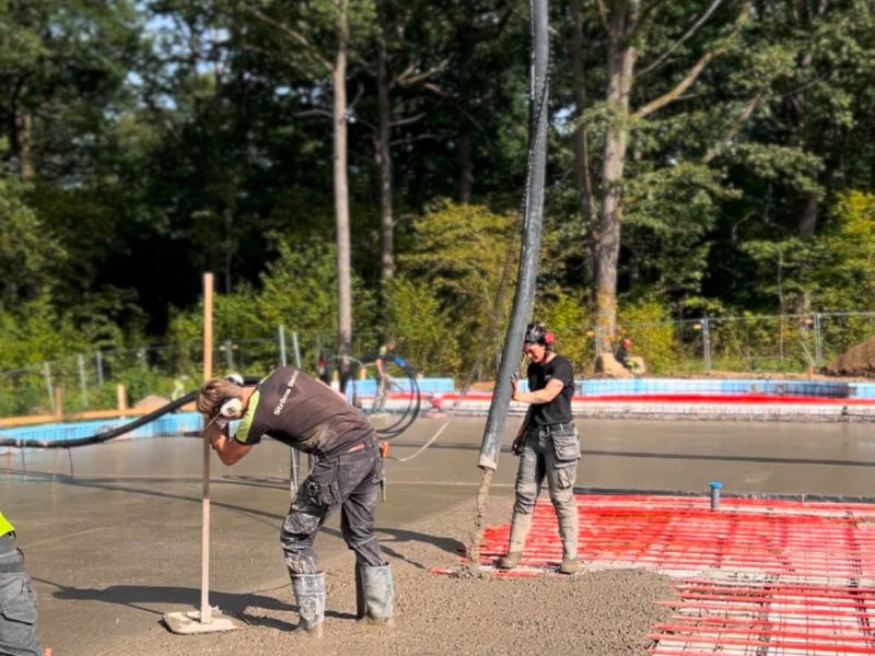 Betongpumpens bom når in över en platta medan betongen dras av