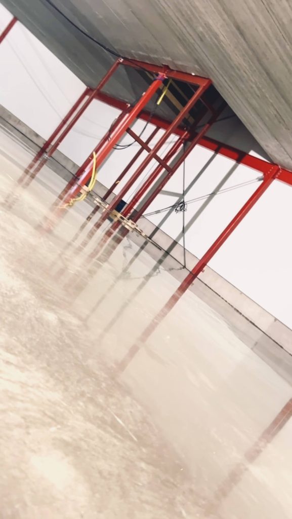 Blankt, nyglättat betonggolv i en industrihall med röda stålpelare