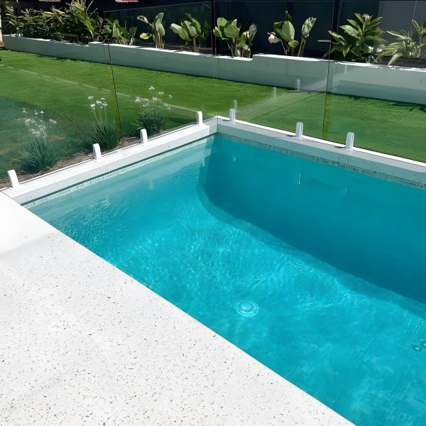 Pool med turkost vatten och ljus poolkant i trädgård